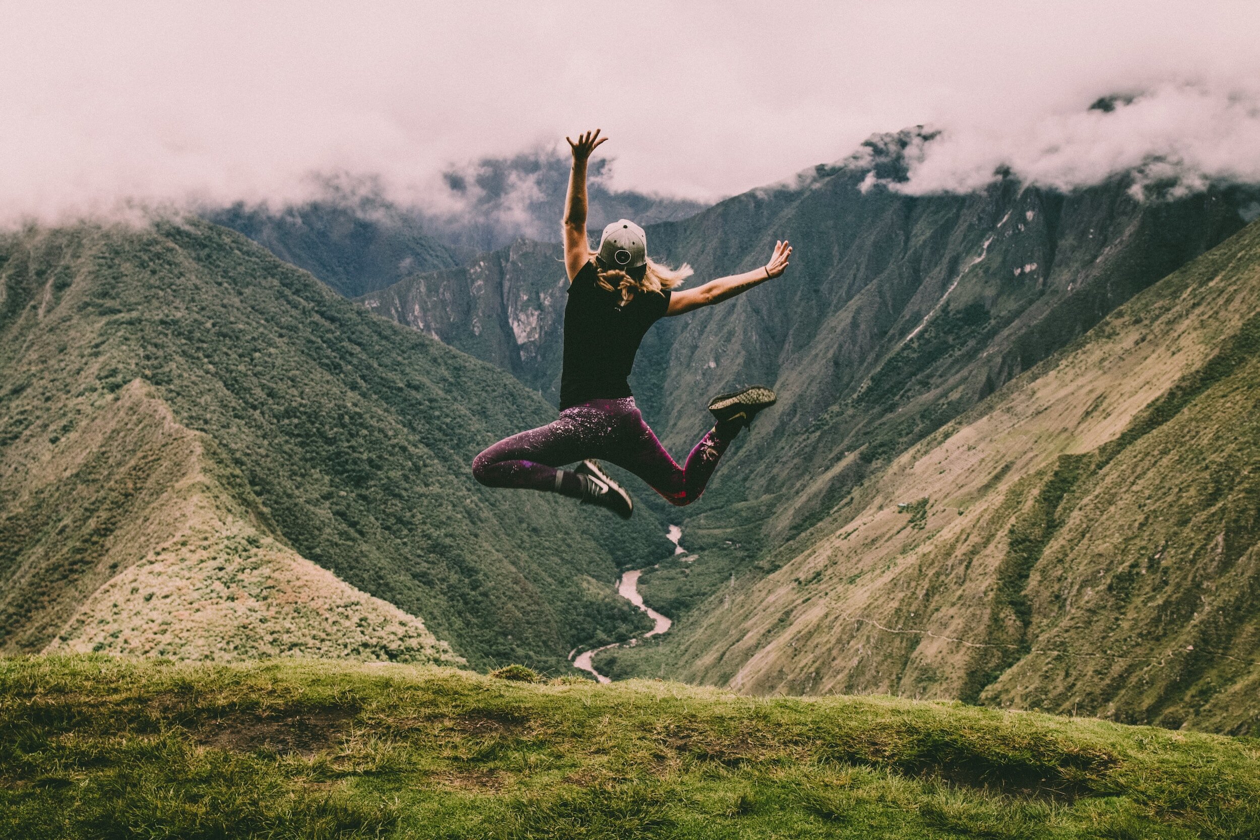 past life healing woman jumping for joy overlooking the green mountains and valley below